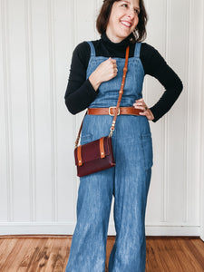 woman wearing leather crossbody bag, with denim overalls and a black tissue turtle neck